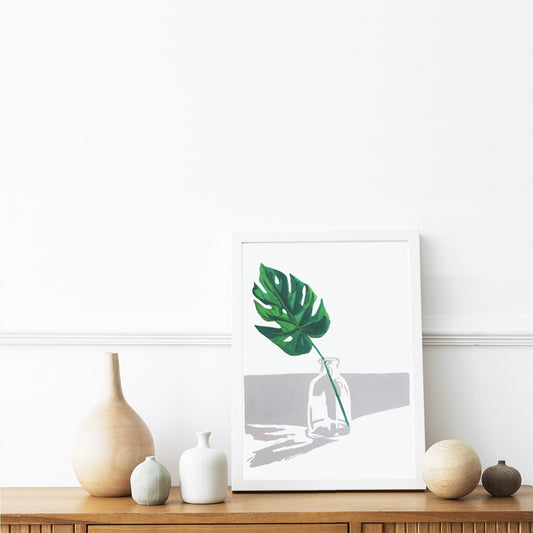 Clean, minimalist design of a monstera leaf in glass bottle in neutral colours in a black picture frame.